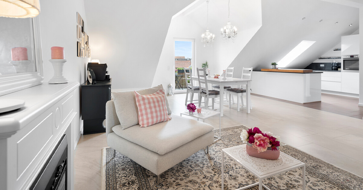 Ein loftartiges Wohnzimmer mit offener Küche, Kamin und gemütlicher Sitzgruppe sowie begeisternden Gauben und bodentiefen Fenstern, Bild aufgenommen für den Immobilienverkauf